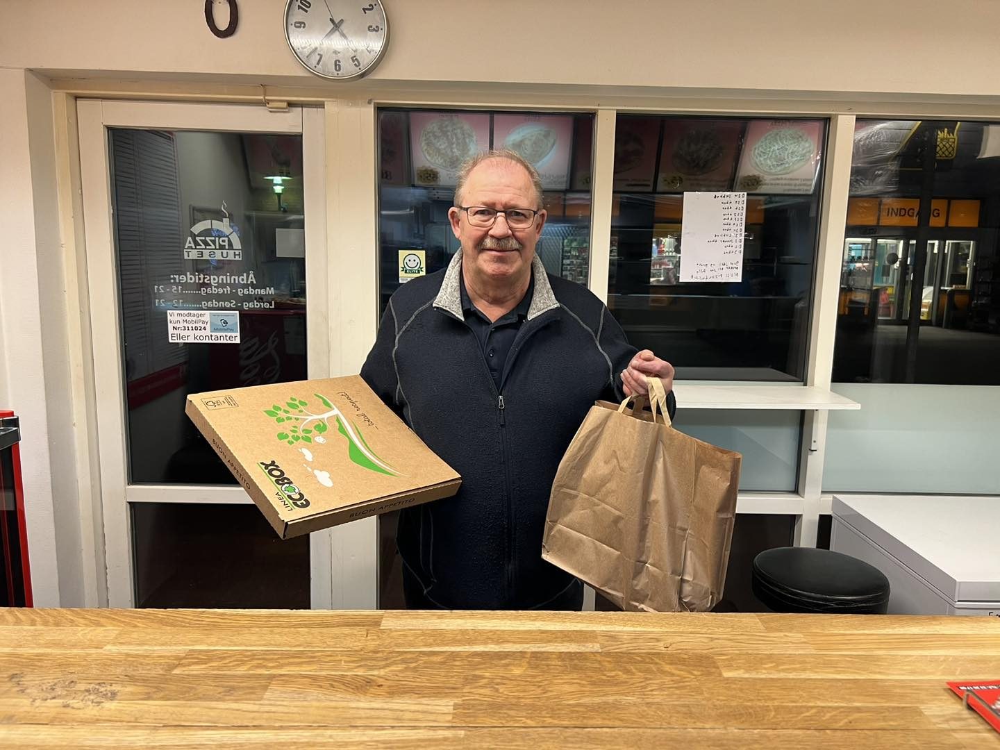 Tilfreds kunde henter pizza og en pose mad i Pizzahuset Holstebro